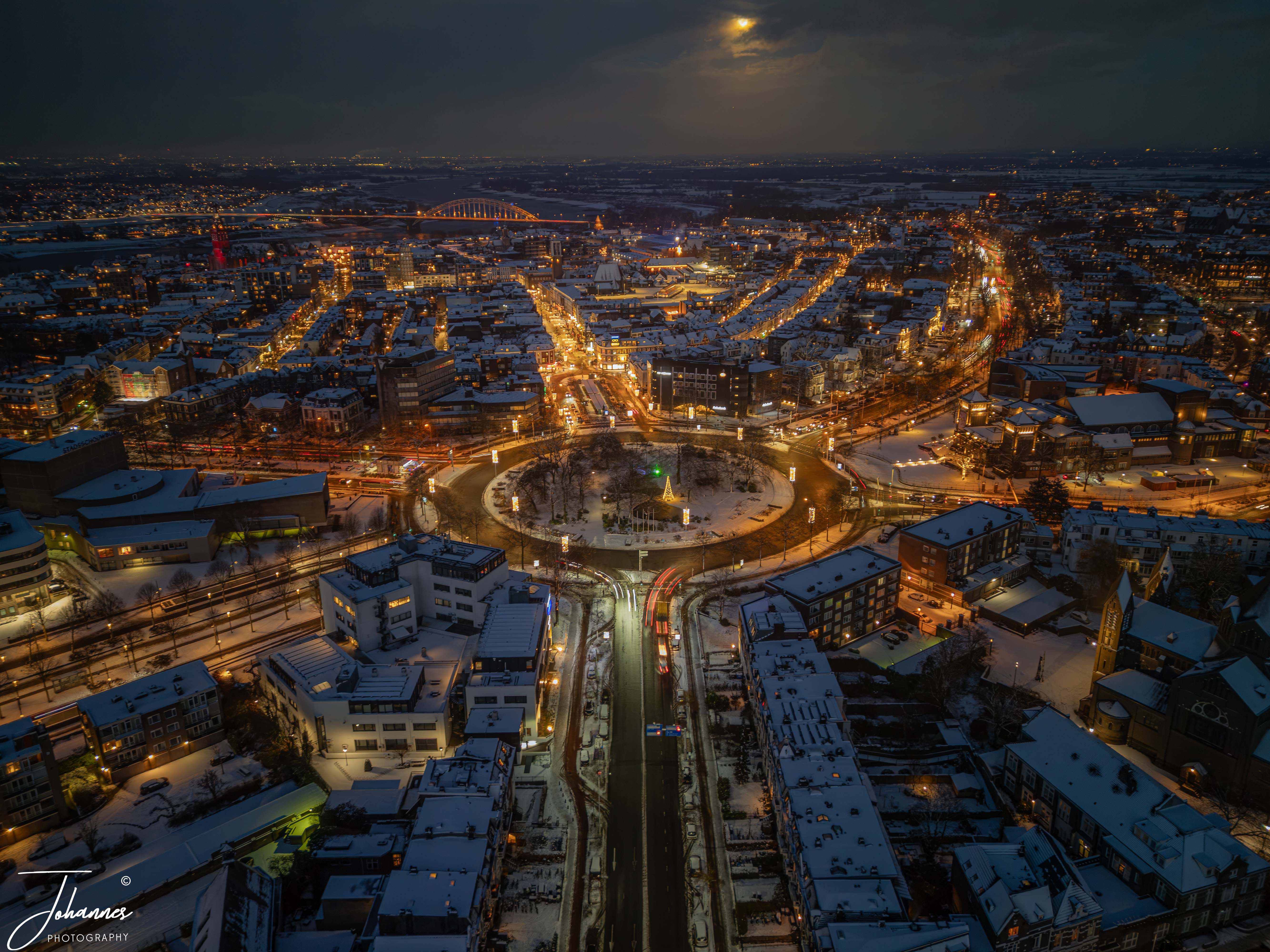 Sunset has nearly completen, a small layer of snow is covering the city (Nijmegen). All the roads have been cleaned and quit some travic is passing by. What a beatifull site of one of the most famous round abouts of the Netherlands.