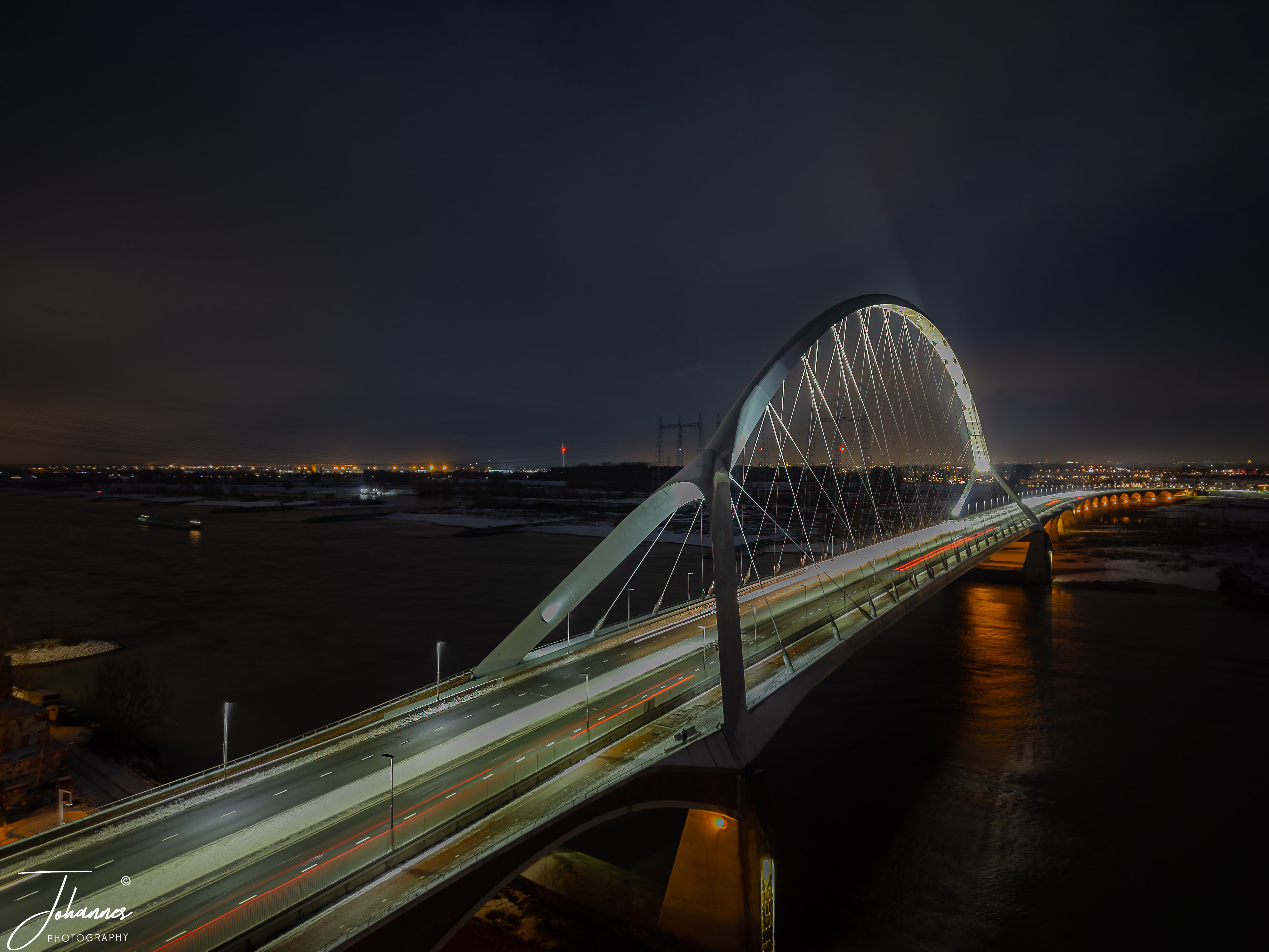 It is the beginning of the year and we have snow. Only a couple of centimeters, but still, everything is in white. Took my drone during bue hour to one of the bridges of Nijmegen, the Oversteek. It is a beautifull bridge increased the shutter speed to have the light stripes over the cars driving by