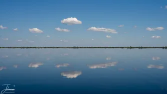 Crossing the lakes of the beautiful Danube Delta under a sunlit, windless sky. We were treated to this mesmerizing moment where the vast blue heavens and floating clouds were perfectly mirrored in the silent water below.