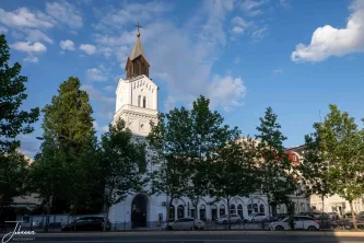 Standing tall in a historic district of Bucharest, this elegant white church with its dark, prominent spire rises above the busy city streets. A striking landmark, it blends architectural heritage with the modern pulse of the capital.